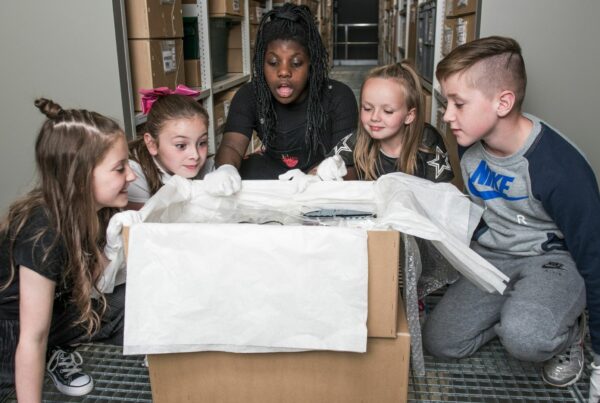 four young school pupils peer into a box of items with a learning assistant at The Burrell Collection