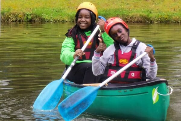 two girls with beaming smiles paddle a canoe