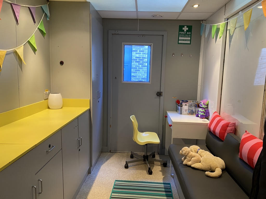 Inside the Camulance is a desk with brightly coloured chair, a sofa with cuddly toys and workspaces