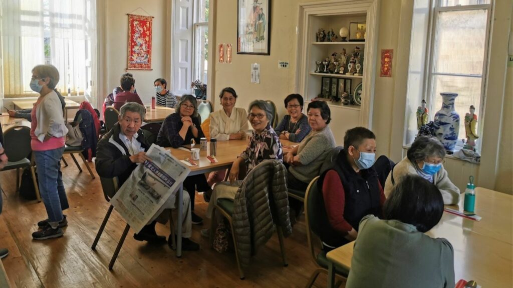 Inside the Wing Hong Centre where a group of older Chinese people are enjoying a chat whilst sitting at large tables