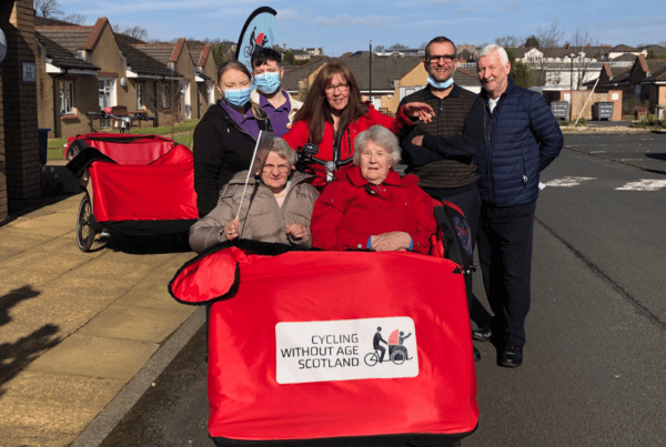 A red trishaw with two elderly ladies in with a group of Care Home Staff standing beside them, photographed at Rutherglen Care Home