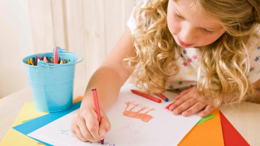 a blonde girl sits at a table colouring in