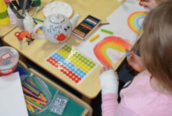 A little girl sits at at a table with arts and crafts painting a rainbow