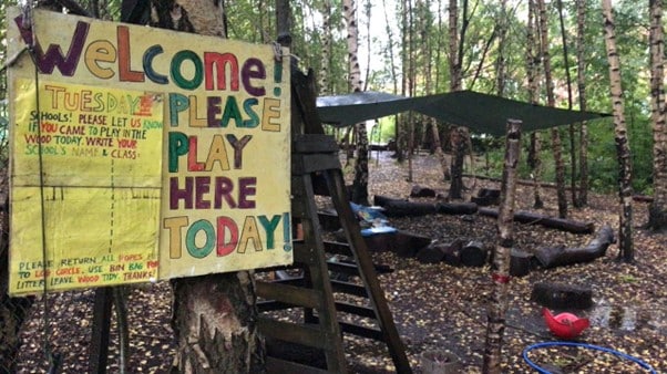 A sign made my children that reads Welcome Please play here today attached to a tree in the Children's Wood