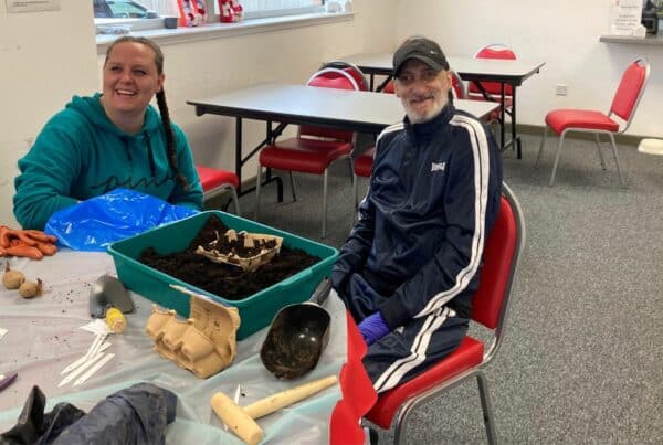 A man and woman at Deafblind Scotland plant seeds in an egg carton whilst sitting indoors at a table.