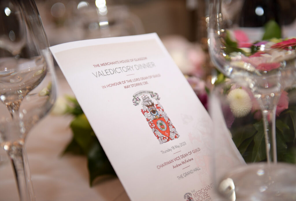 The Menu for the Valedictory Dinner sits on the table amongst a pink and white floral arrangement and glasswear